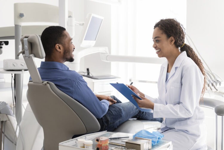 Smiling female dentist filling medical chart, talking to patient